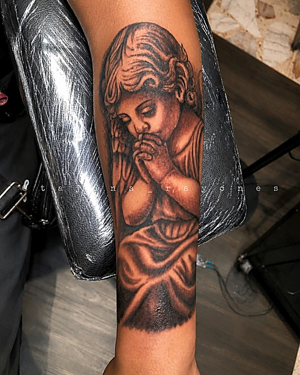 Ángel en oración en realismo negro y gris, en el antebrazo