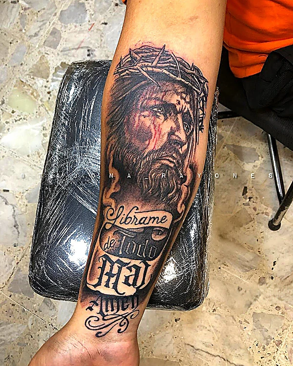 Rostro de Cristo con corona de espinas y la frase Líbrame de todo mal, en el antebrazo