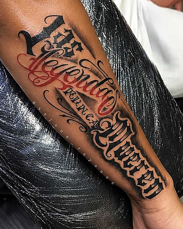 Lettering gótico en negro con palabras en rojo, a lo largo del antebrazo