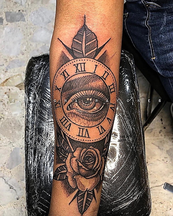 Reloj con números romanos, un ojo al centro y una rosa, en el antebrazo